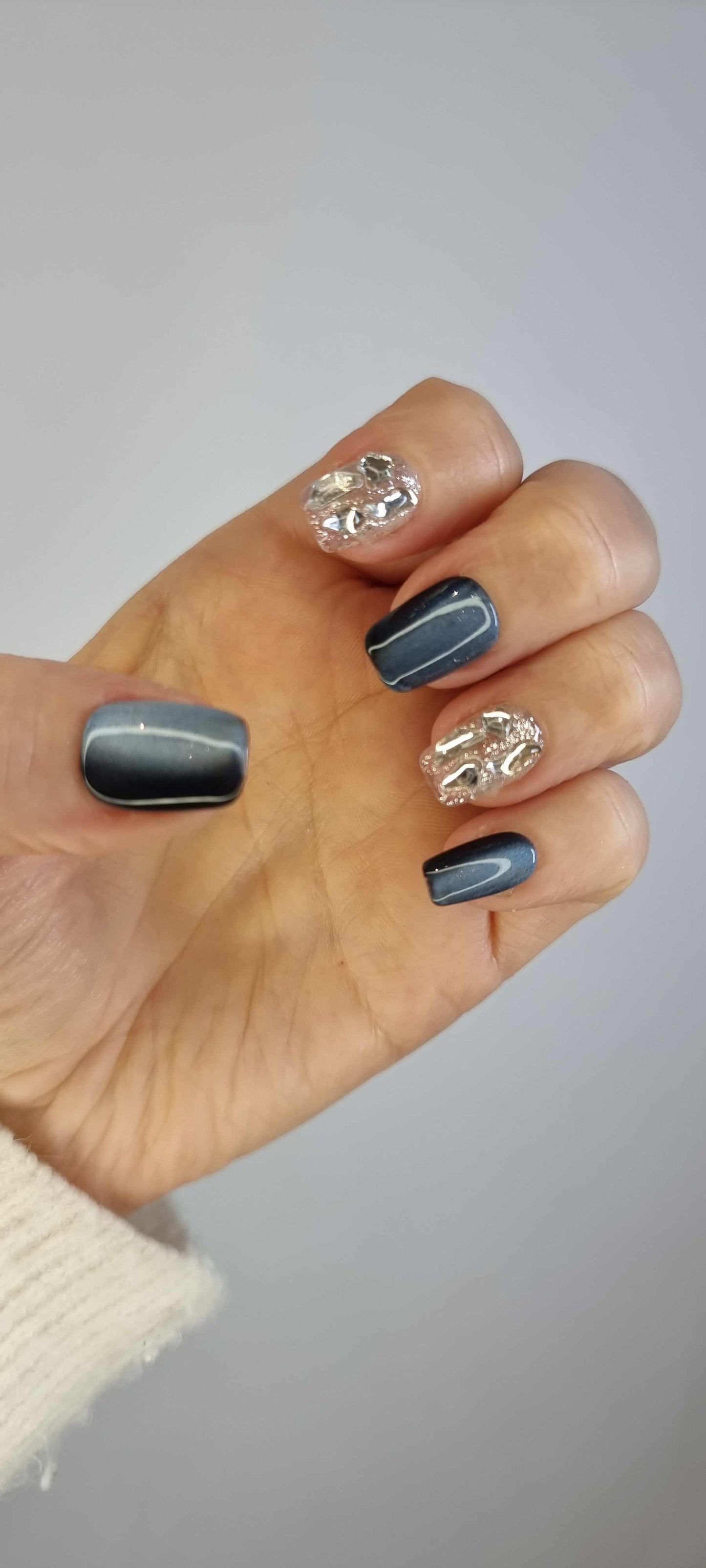 A model's hand wearing the modern Days in Dubai press-on nails, showcasing the unique textured chrome design.