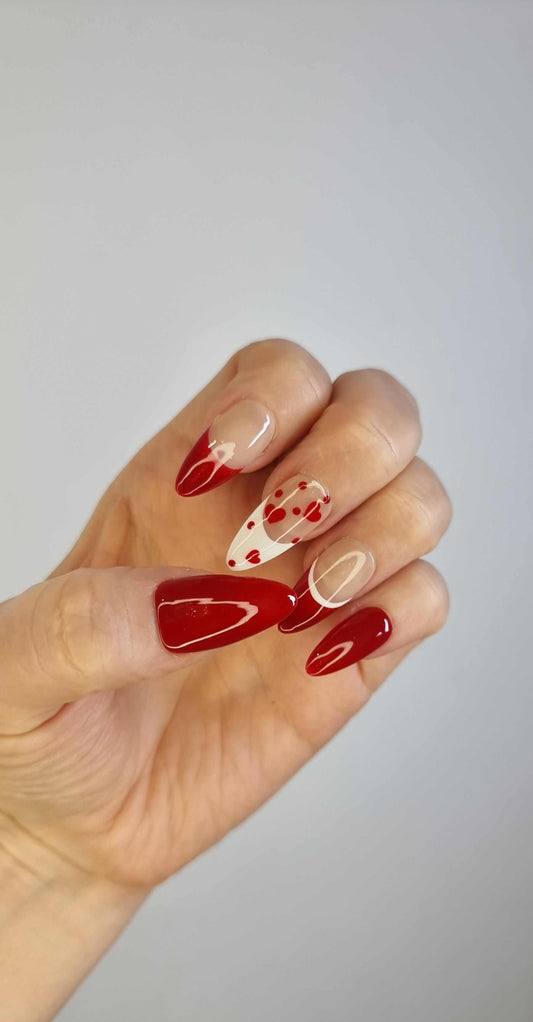 A model's hand showcasing the Holiday Romance press-on nails, with a close-up on the intricate red heart and French tip details.