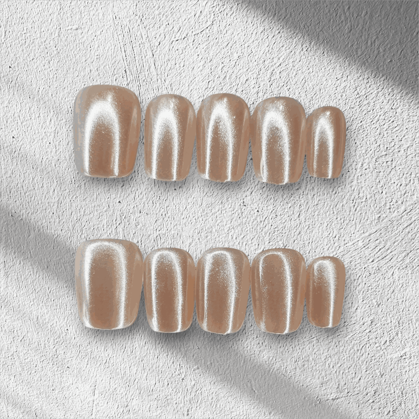 Pearls of Bahrain press-on nails in a short square shape, featuring an elegant, pearlescent champagne shimmer finish, displayed on a textured background.