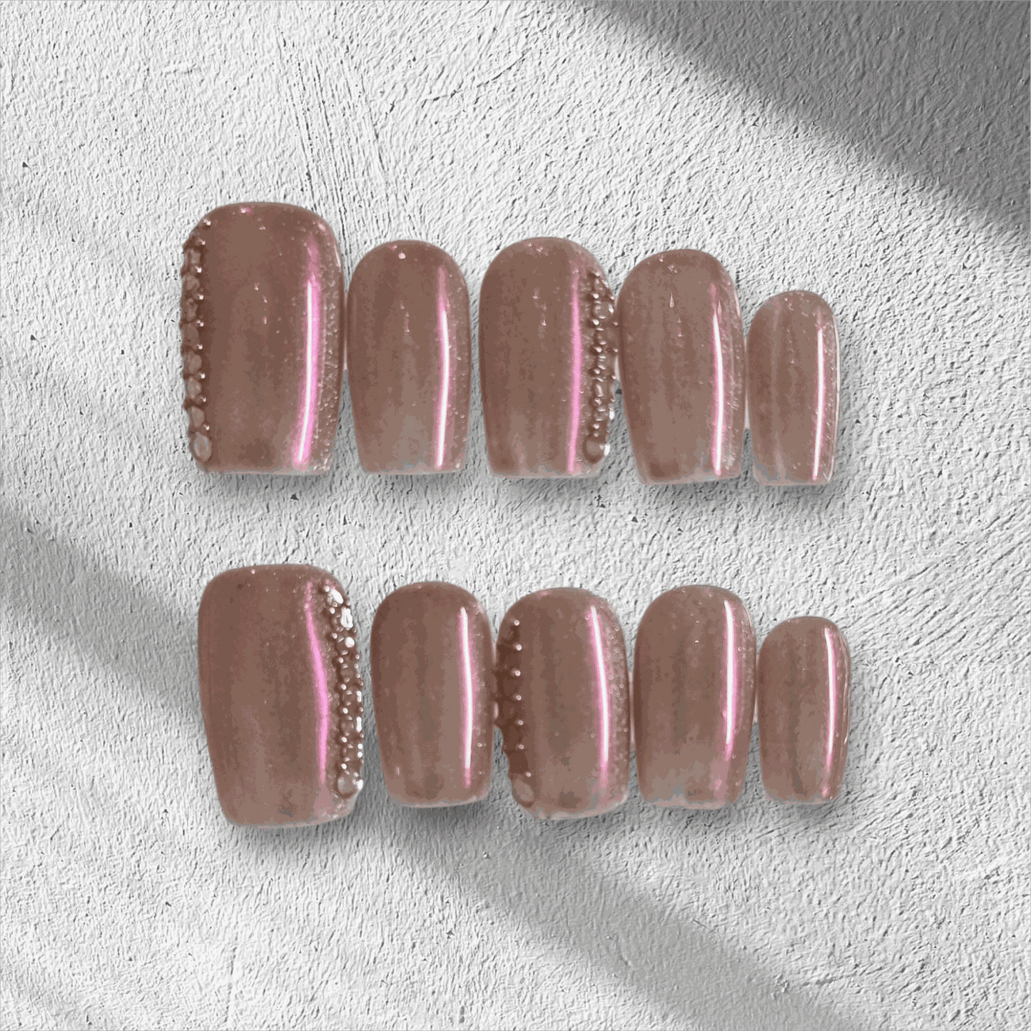 A set of false press-on nails in a sheer, glossy nude color. Each nail is decorated with a vertical line of alternating small white pearls and clear rhinestones.