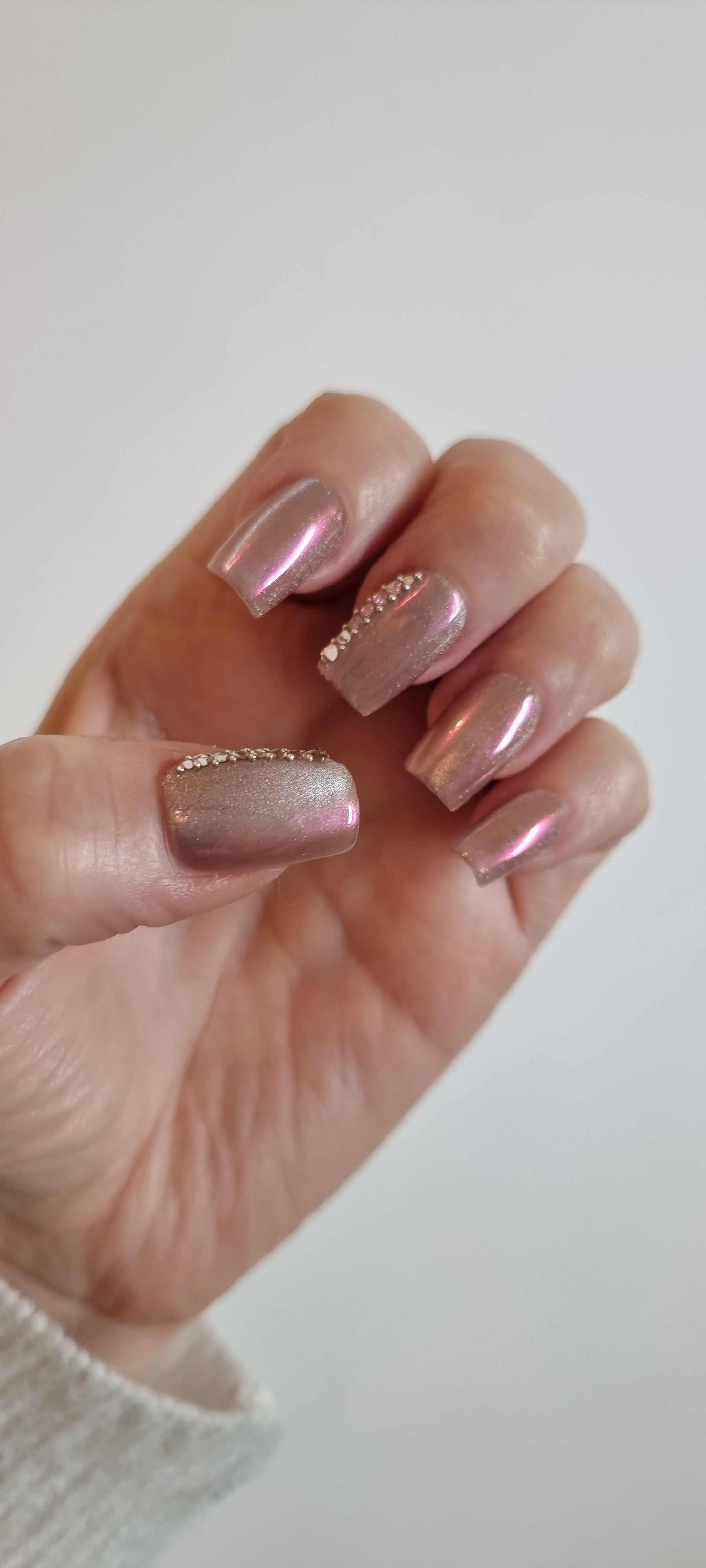 A set of false press-on nails in a sheer, glossy nude color. Each nail is decorated with a vertical line of alternating small white pearls and clear rhinestones.