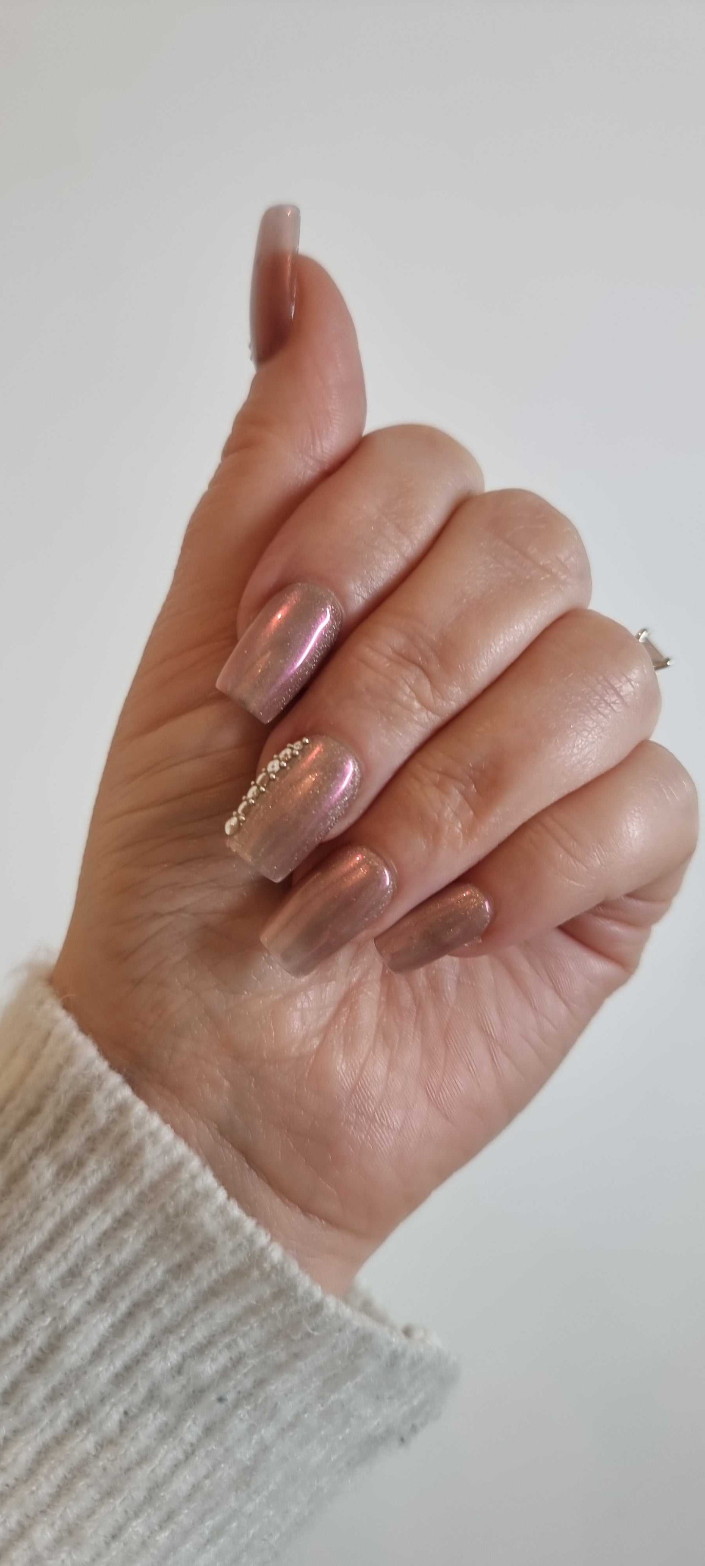 A set of false press-on nails in a sheer, glossy nude color. Each nail is decorated with a vertical line of alternating small white pearls and clear rhinestones.