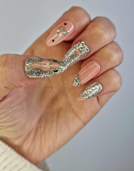 A set of nude almond-shaped press-on nails. The nails are decorated with dangling chain-like rhinestones and small star accents.