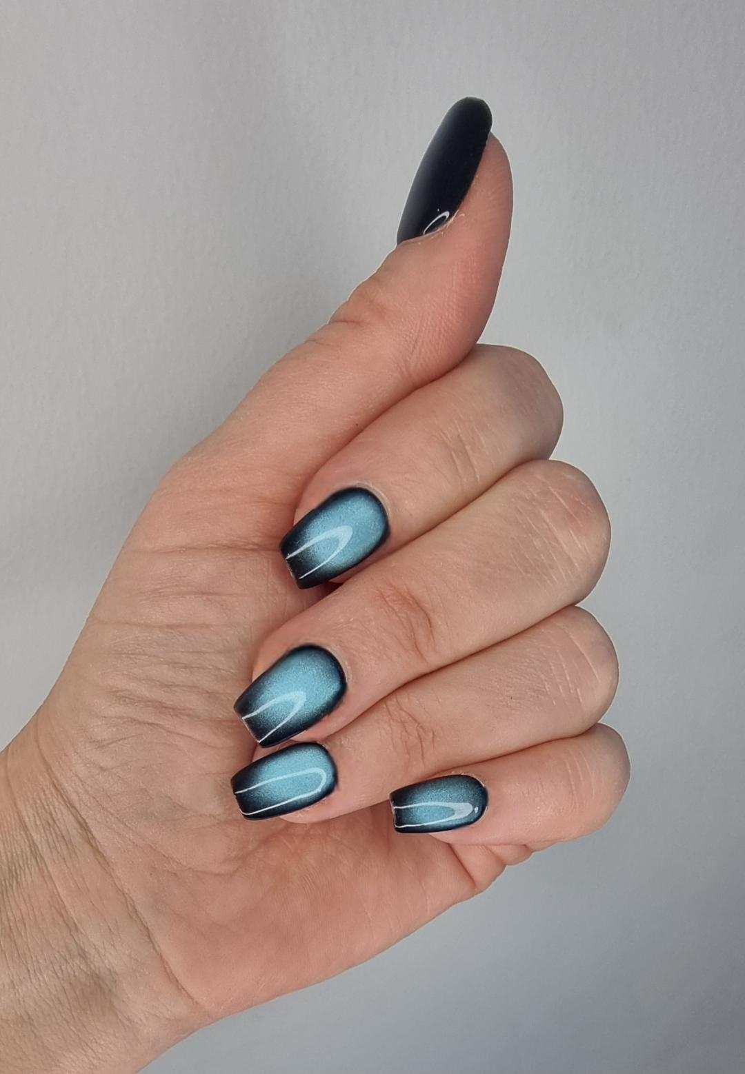 hand with blue magnetic shimmer Yalla manicure nails on grey background