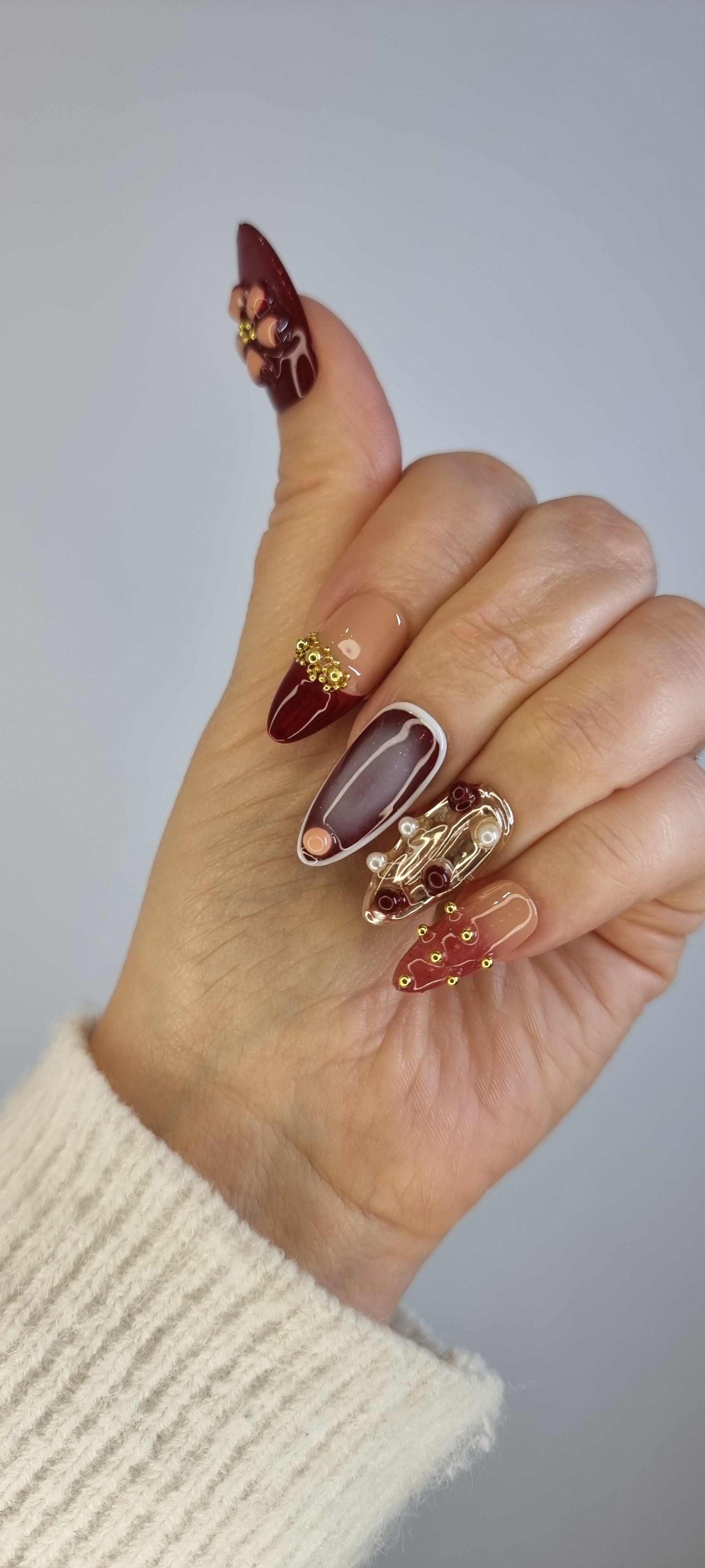A model's hand wearing the intricate Arabian Nights press-on nails, showcasing the detailed 3D floral art and rich color palette.