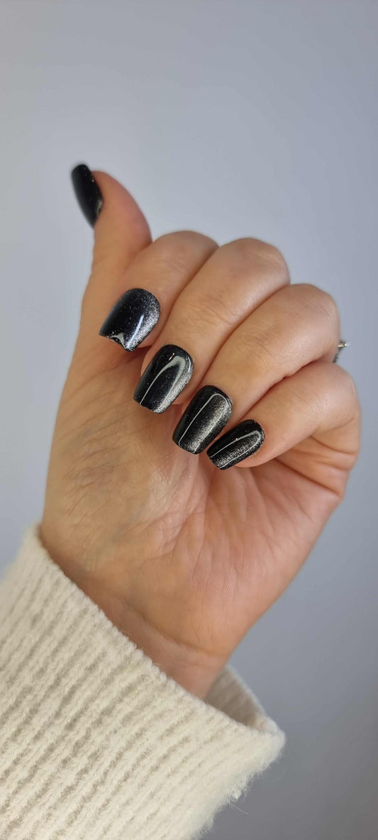 A model's hand wearing the sophisticated Deira Dusk press-on nails, showcasing the sparkling black glitter effect.