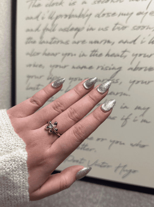 Hand with glittery nails wearing a gold ring with a green gemstone, in front of handwritten text.