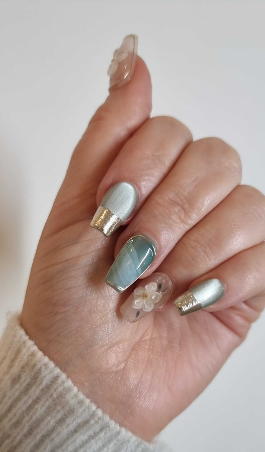 A model's hand wearing the sophisticated Glam in GCC press-on nails, showcasing the unique chrome French tip and 3D floral details.