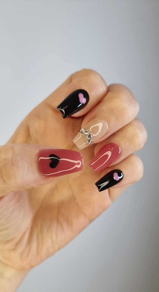A model's hand showcasing the dramatic Hind press-on nail manicure with its bold red, black, and rhinestone details.