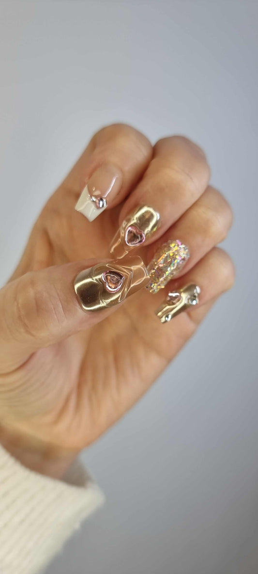 Hand wearing Jawhara Glow long coffin press-on nails with a nude base, gold chains, and delicate pearl details.