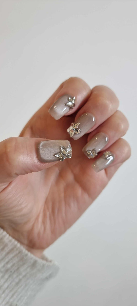 Hand wearing Jeddah Glow pearlescent nude press-on nails, showcasing the unique 3D silver flower and leaf charm on the ring finger.
