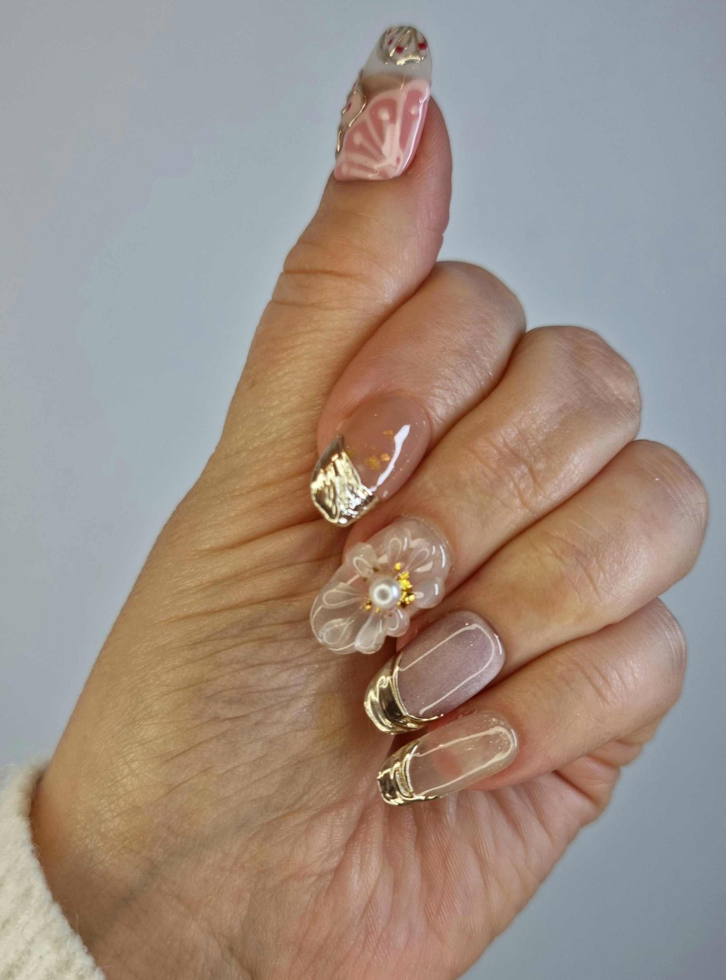 Hand wearing Jenny press-on nails by Nail Addict, showcasing the detailed artistry, 3D flower charm, and polished gold accents.