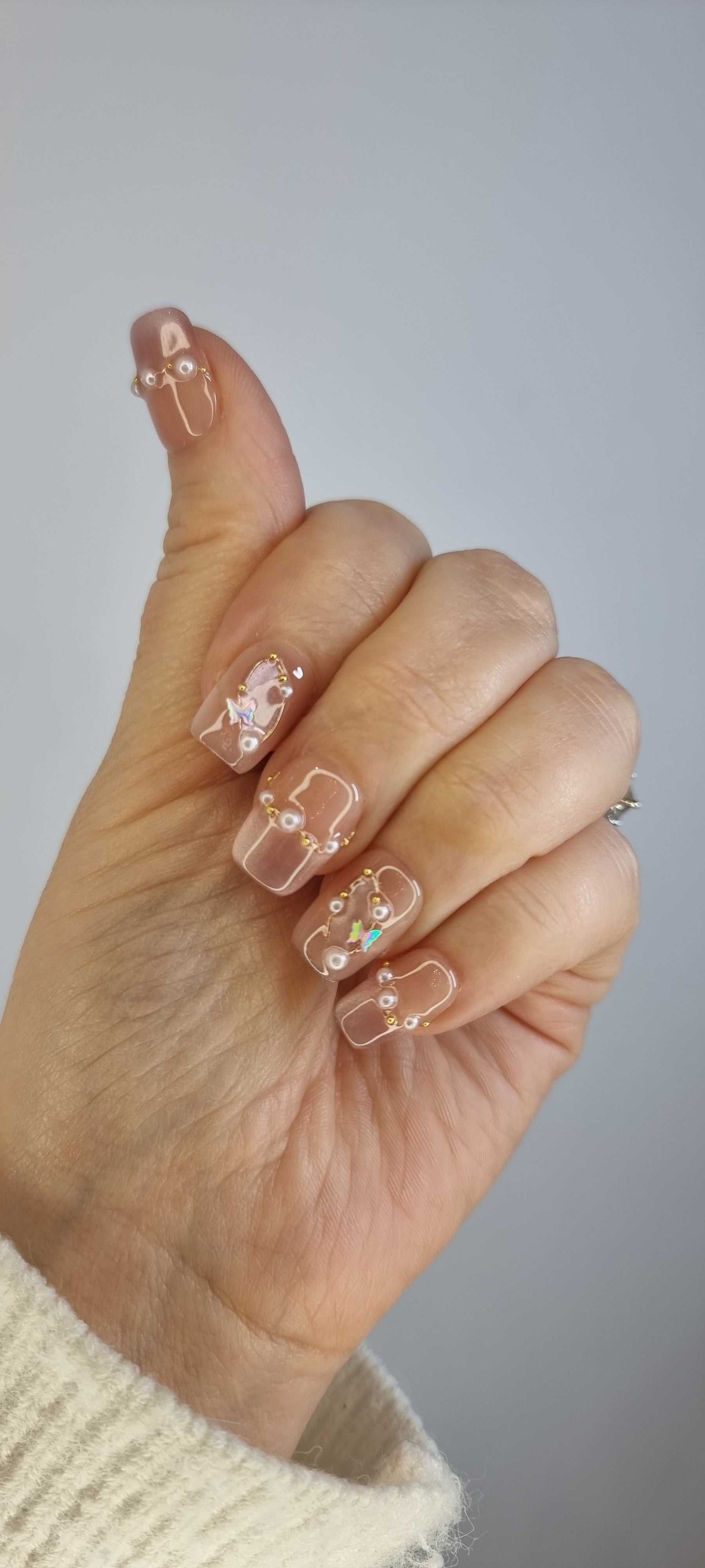 Hand wearing Khawla brown and nude press-on nails by Nail Addict, featuring elegant gold chains and pearl accents on each nail.