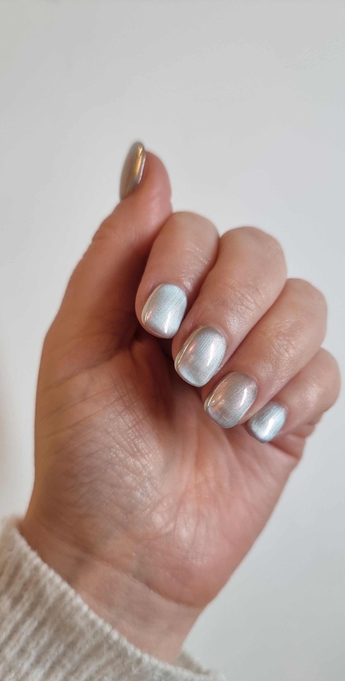 Hand wearing Lujain pearlescent gray-silver short oval press-on nails.