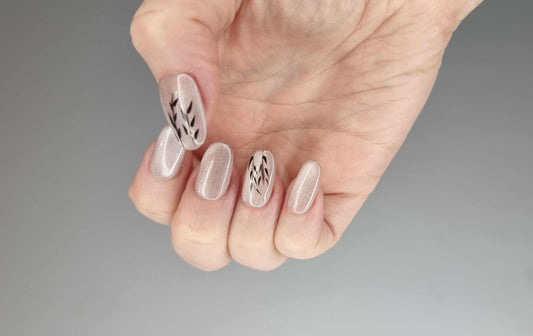 Hand wearing Marwa press-on nails with a glossy nude finish and black botanical designs.