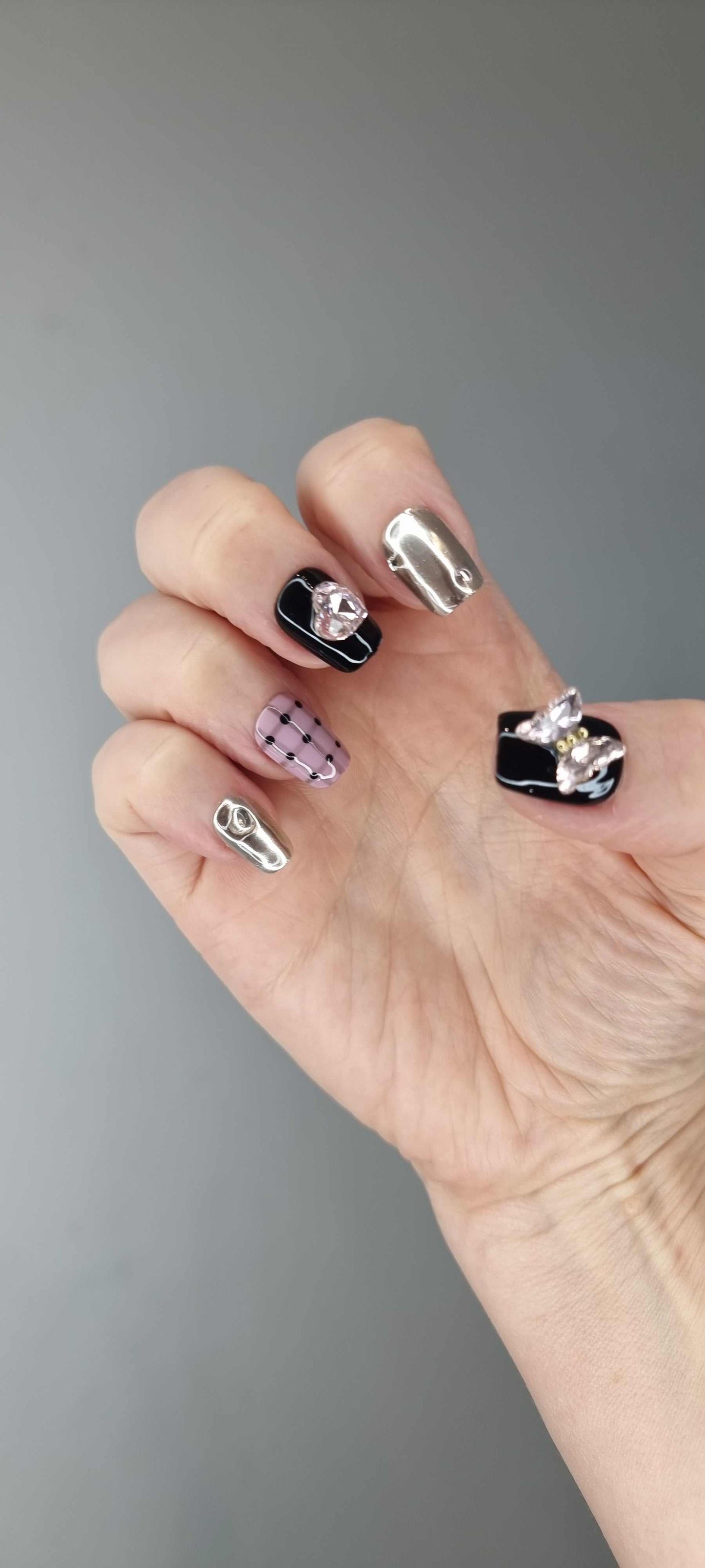 Hand wearing Maysoon coffin press-on nails in black, silver chrome, pink plaid, and polka dots.