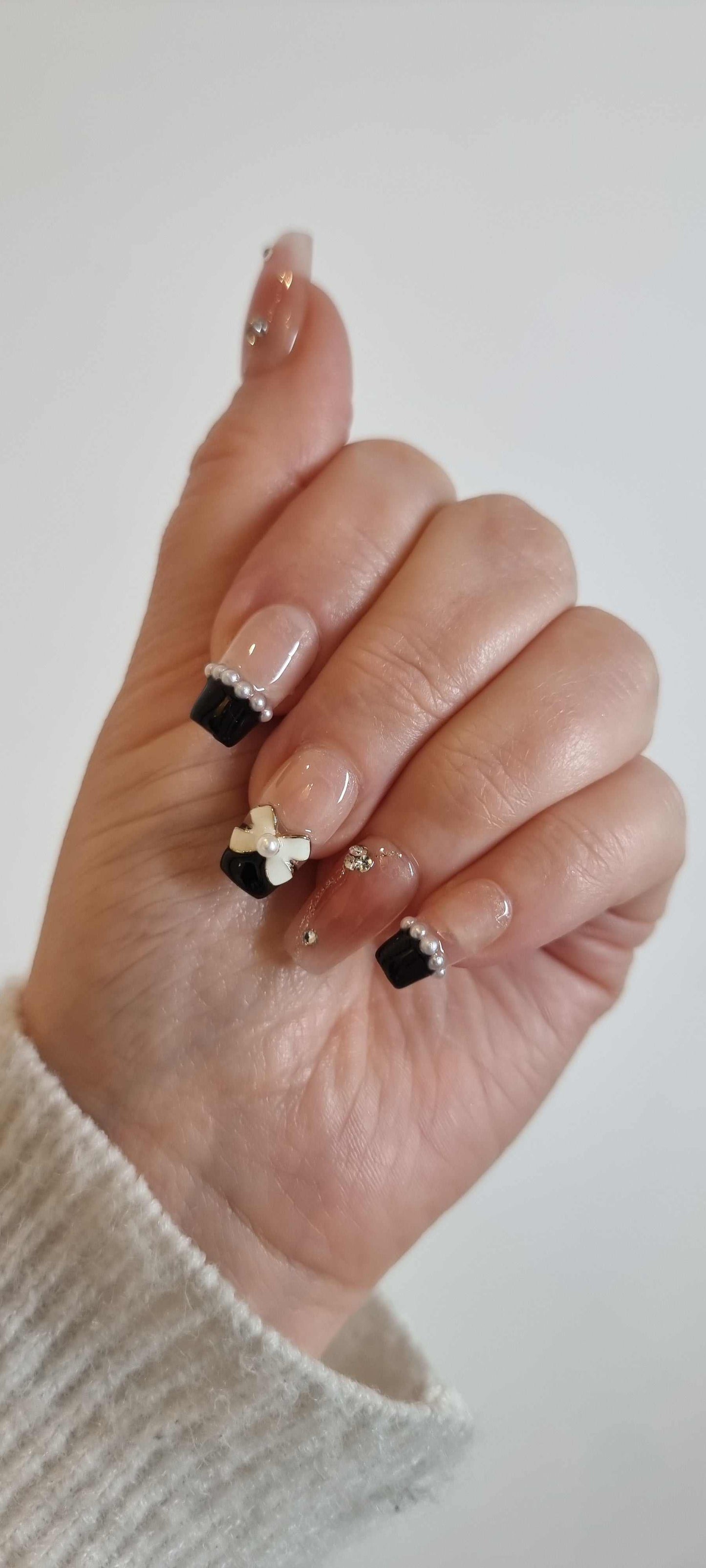 Close-up of Mecca Magic French tip square press-on nails with bow and pearls by Nail Addict.