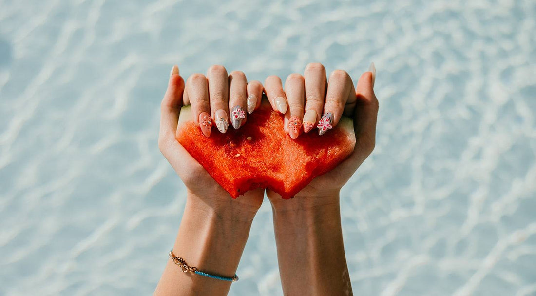 A woman's hands with a beautiful manicure holding a heart-shaped piece of watermelon, representing the love and care behind the creation of Nail Addict's press-on nails.