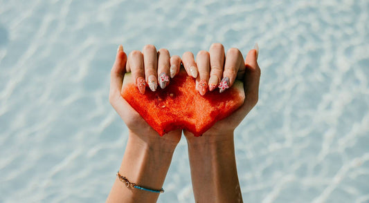 A woman's hands with a beautiful manicure holding a heart-shaped piece of watermelon, representing the love and care behind the creation of Nail Addict's press-on nails.