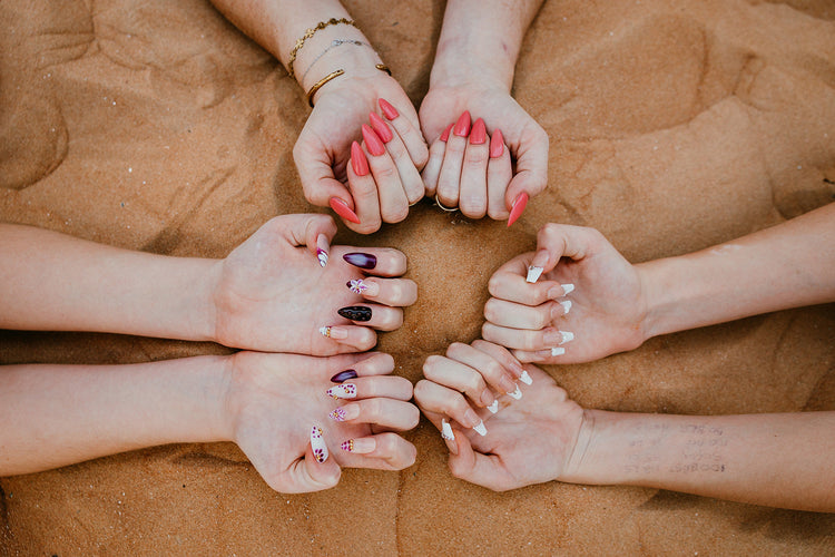Group of hands displaying a variety of manicures including classic coral pink and decorative white nail art against a natural sand background, showcasing professional nail products in the UAE.