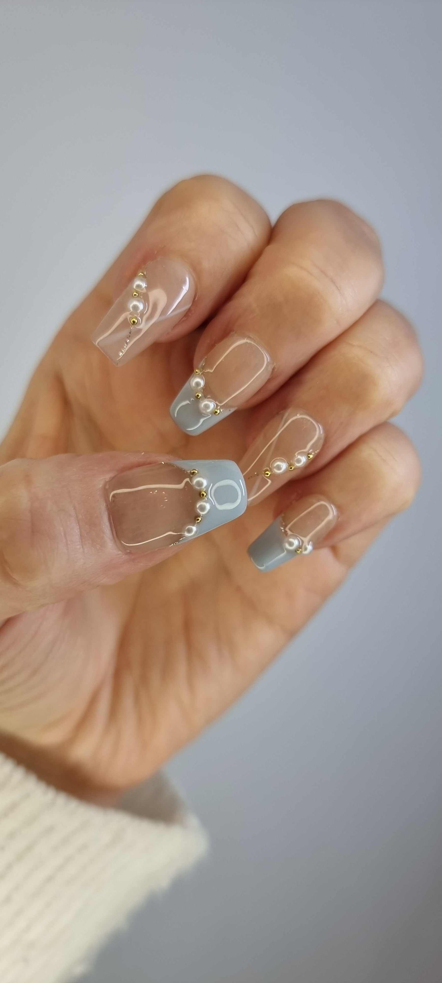 A model's hand wearing the chic Fadwa blue French tip press-on nails, showcasing the elegant pearl accents.