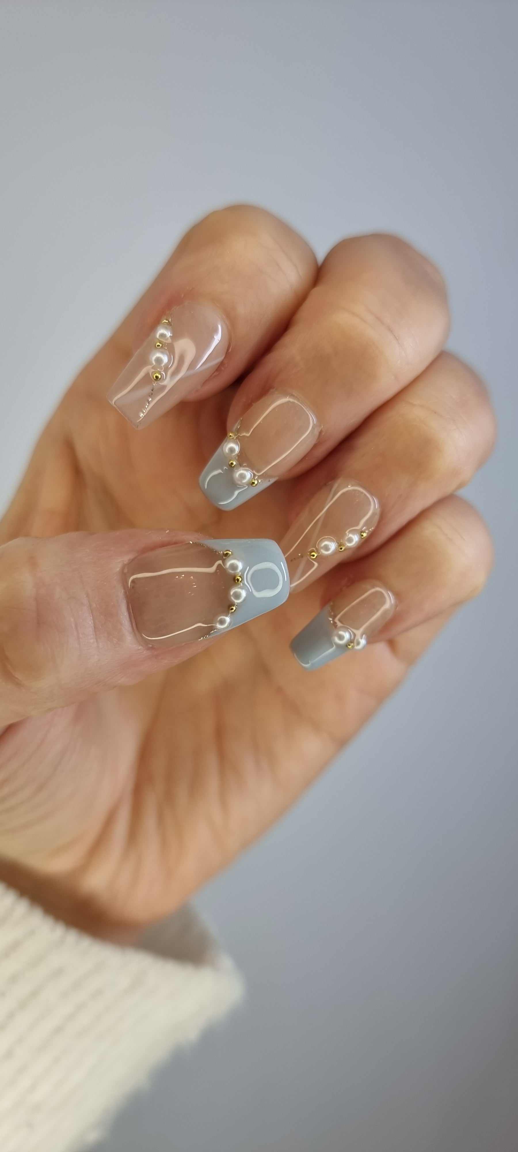 A model's hand wearing the chic Fadwa blue French tip press-on nails, showcasing the elegant pearl accents.