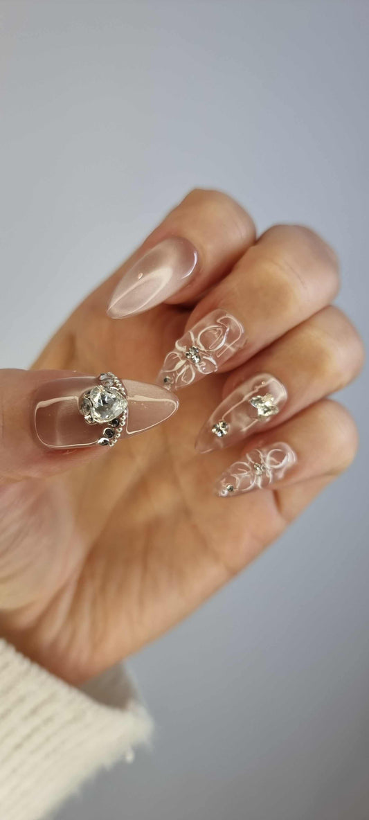 Hand wearing Noor short square press-on nails with a pink and white abstract pattern, accentuated with pearls and gold glitter.