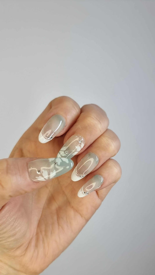 A set of glossy, translucent off-white press-on nails with a pearlescent finish. The nails are decorated with small silver rhinestones and white or iridescent pearls.
