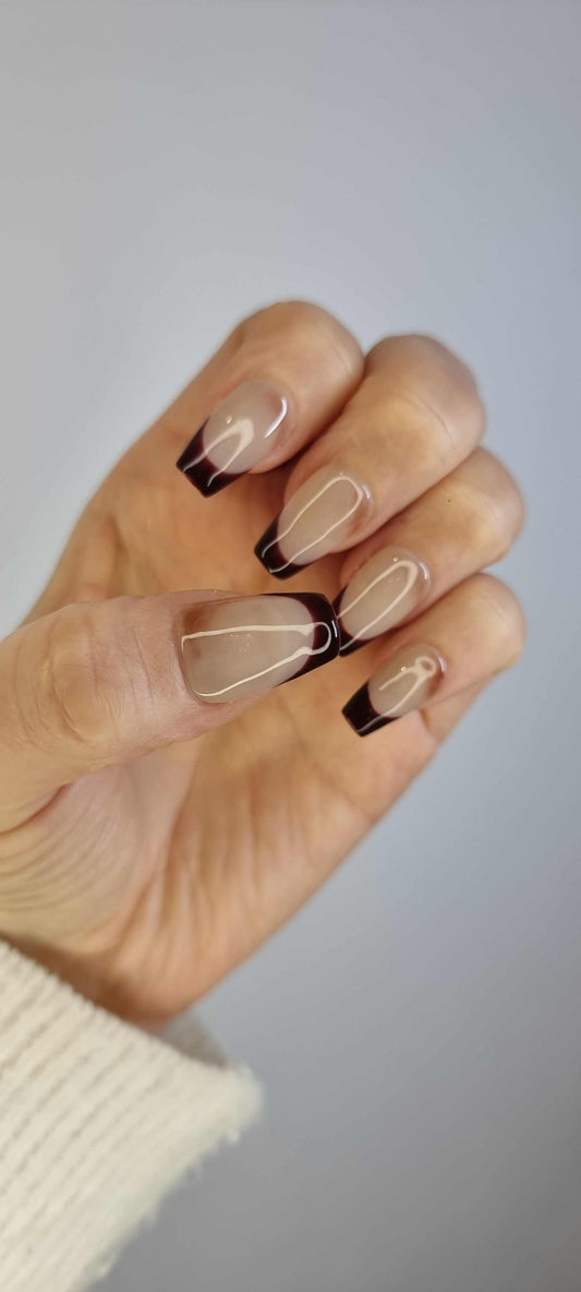 A model's hand wearing the modern Riham press-on nails, showcasing the elegant brown outline on the long coffin shape.