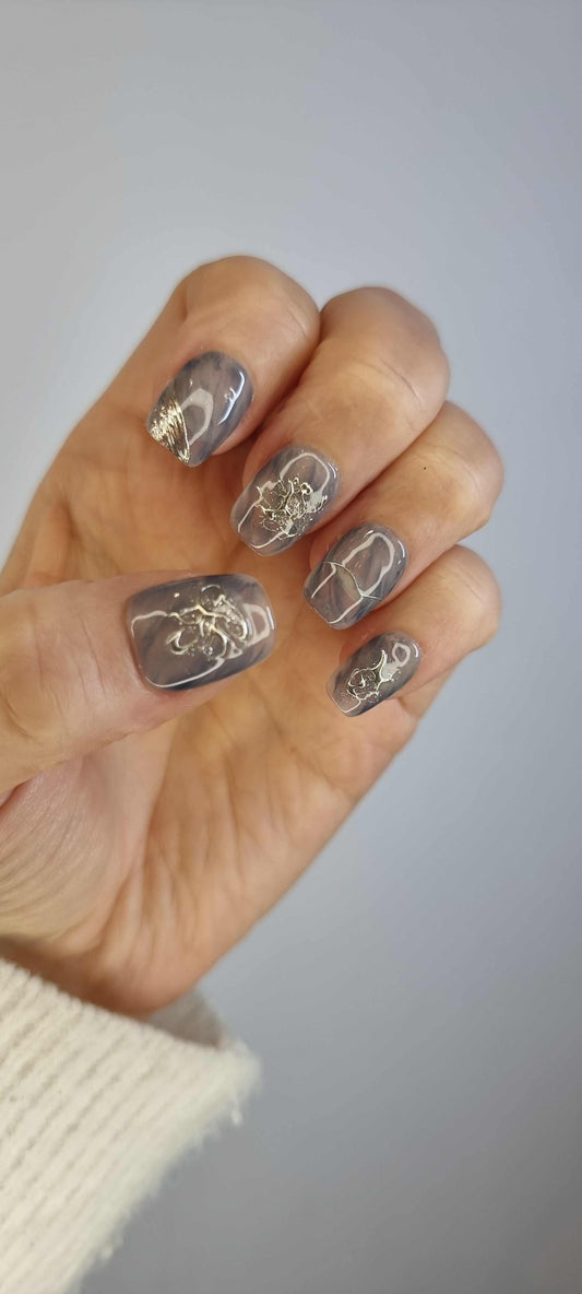 The Shaden press-on nails photo, featuring a translucent smoky grey base with raised 3D metallic silver swirl art on a short square shape.