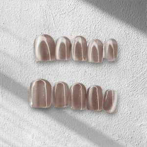 Nude beige glossy press-on false nails set on textured white surface with soft shadow lighting