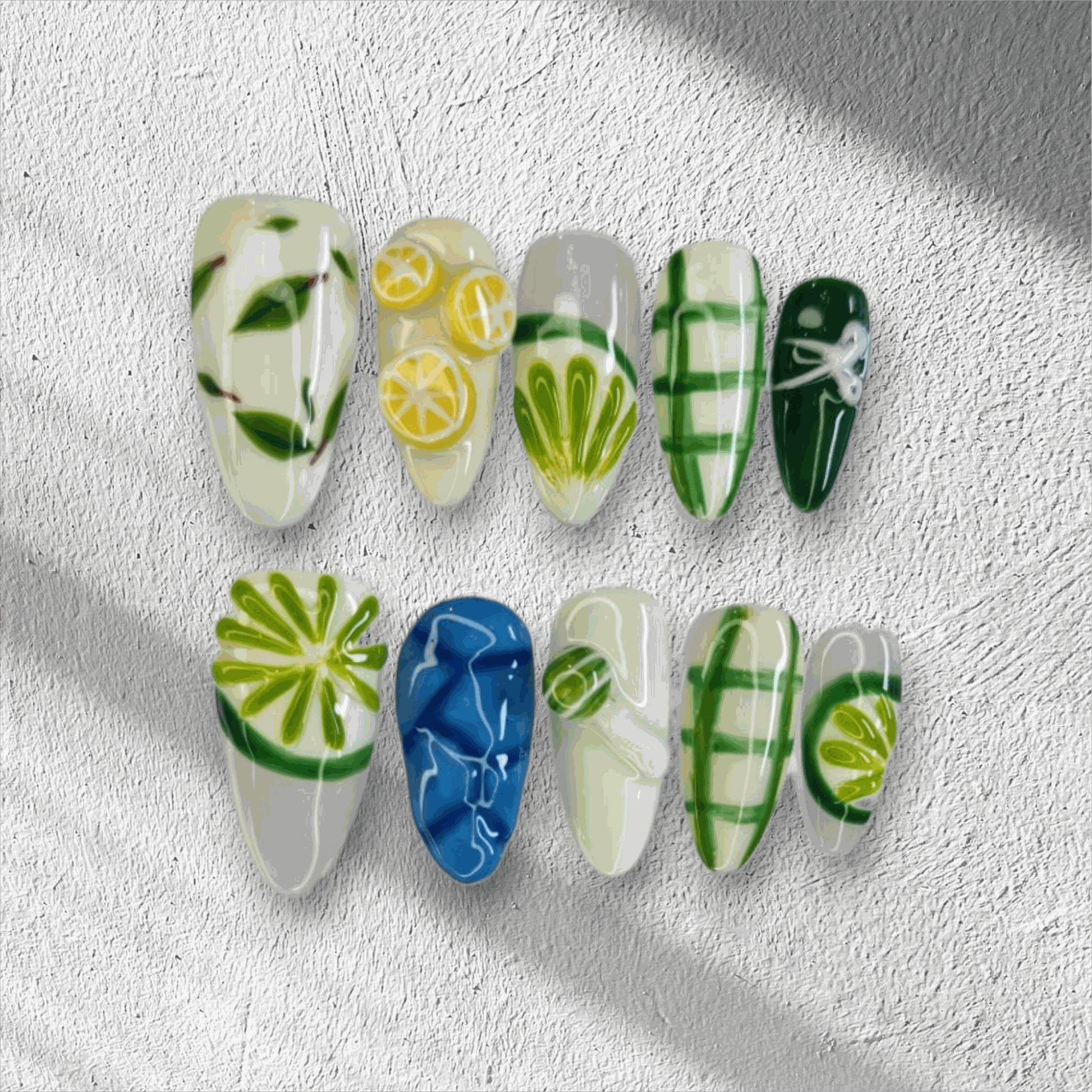 The Al Ain Allure press-on nail set in a long almond shape, featuring intricate 3D citrus and leaf art on a mix of white, green, and blue nails.