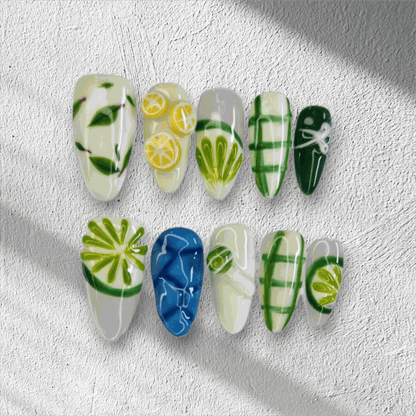 The Al Ain Allure press-on nail set in a long almond shape, featuring intricate 3D citrus and leaf art on a mix of white, green, and blue nails.