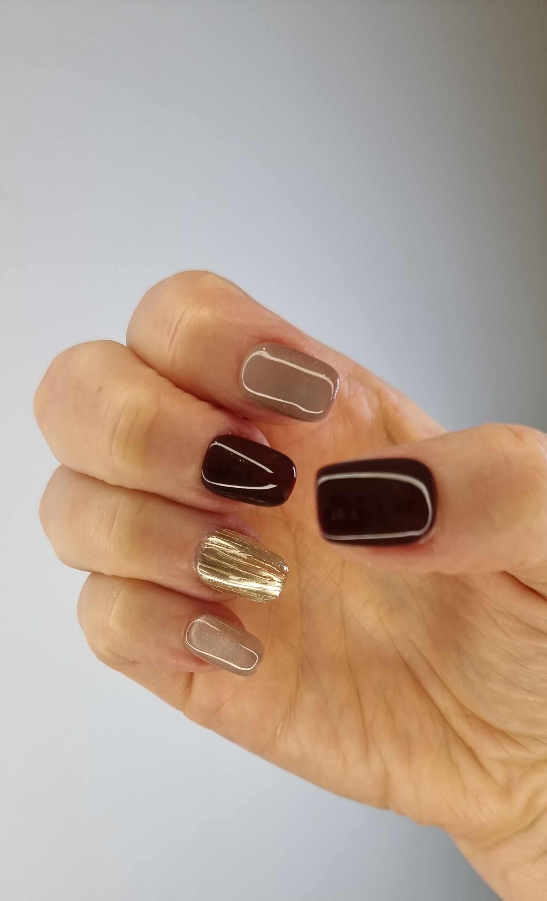 A model's hand wearing the sophisticated Al Khobar Chic press-on nails, showcasing the rich brown and textured gold design.