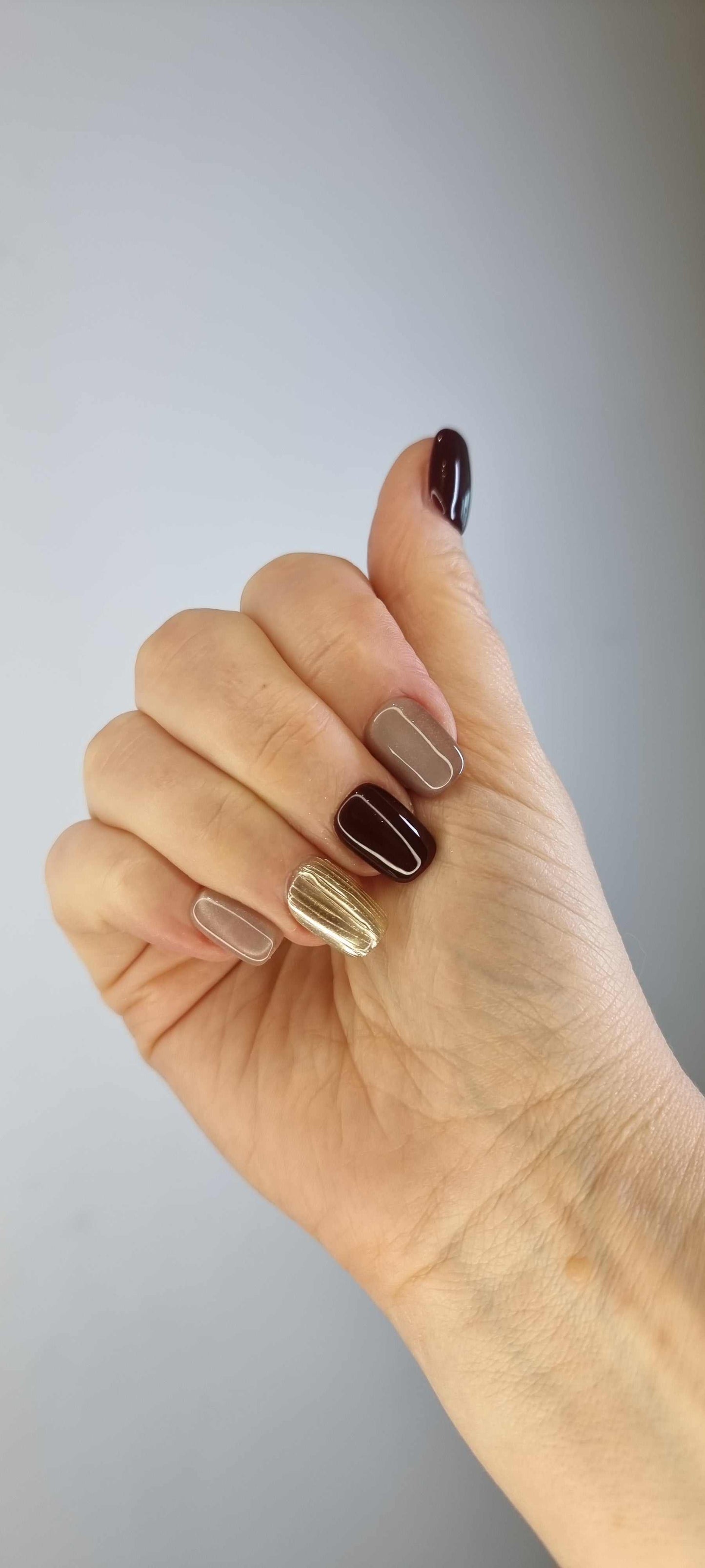 A model's hand wearing the sophisticated Al Khobar Chic press-on nails, showcasing the rich brown and textured gold design.