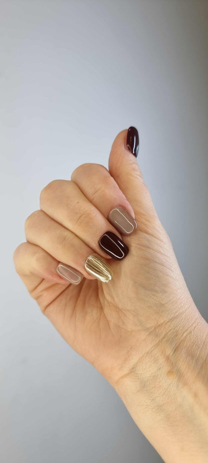 A model's hand wearing the sophisticated Al Khobar Chic press-on nails, showcasing the rich brown and textured gold design.