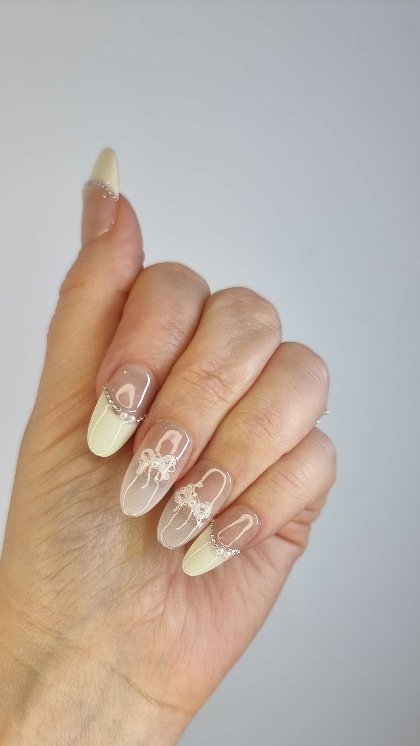 A close-up of the Aseel press-on nail manicure, highlighting the sophisticated French tip and 3D bow design.