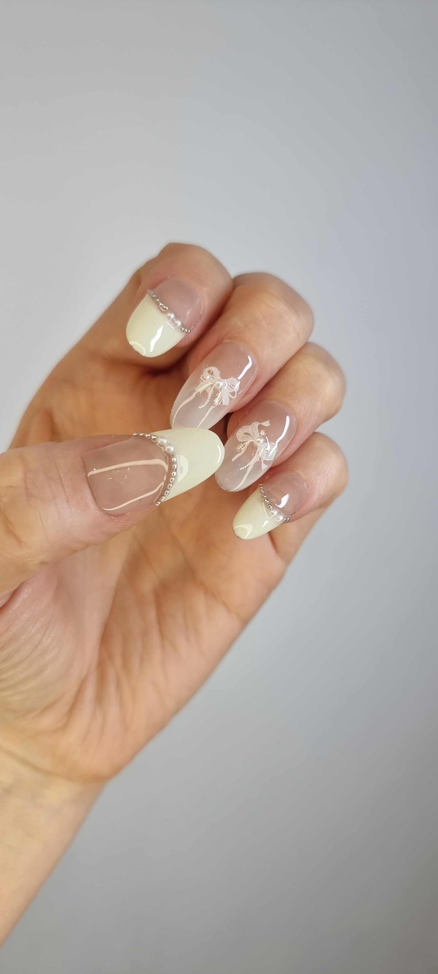 A model's hand wearing the elegant Aseel French manicure press-on nails, showcasing the delicate 3D bow and pearl accents.
