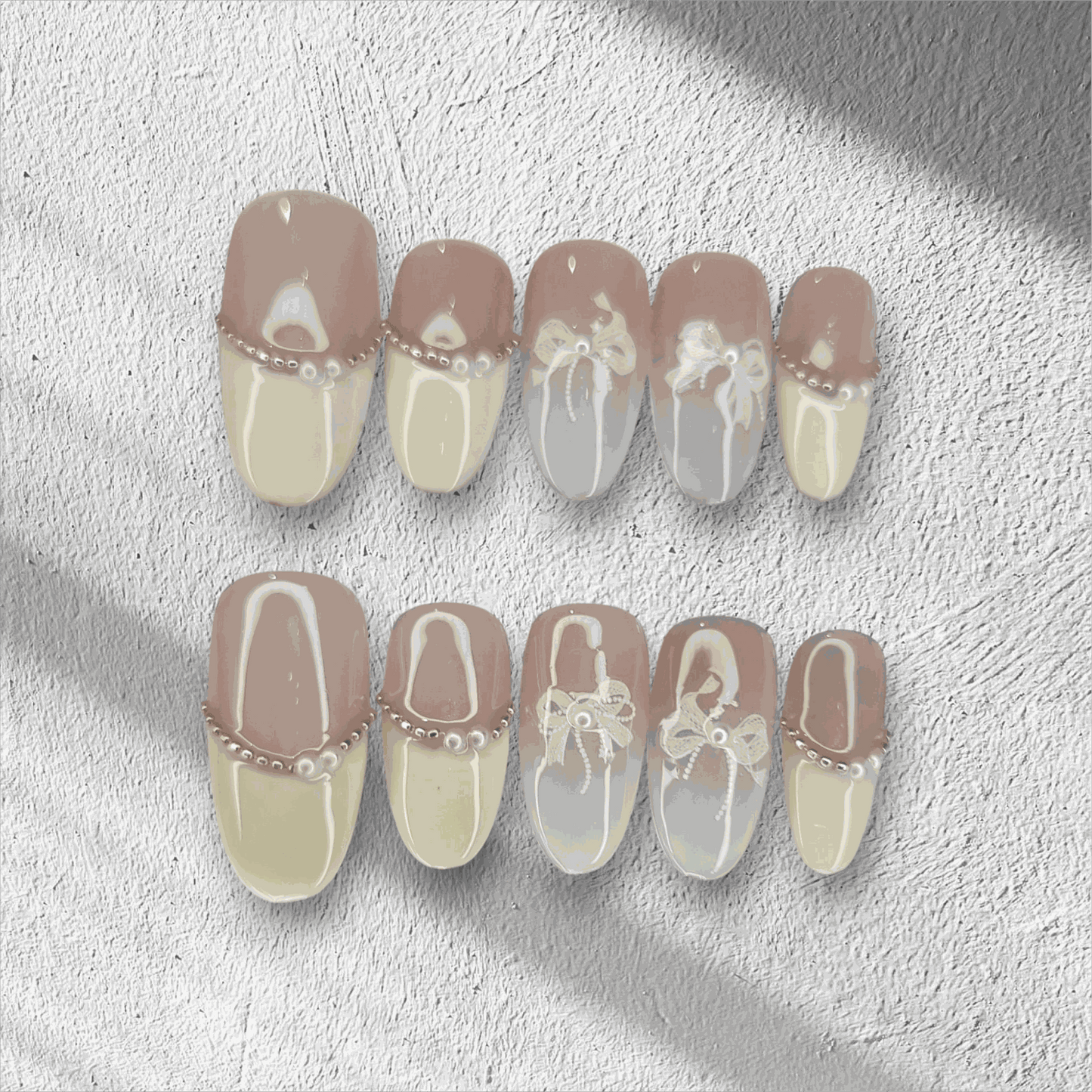 The Aseel press-on nail set in a medium round shape, featuring a classic French manicure design with 3D white bows and pearl details.