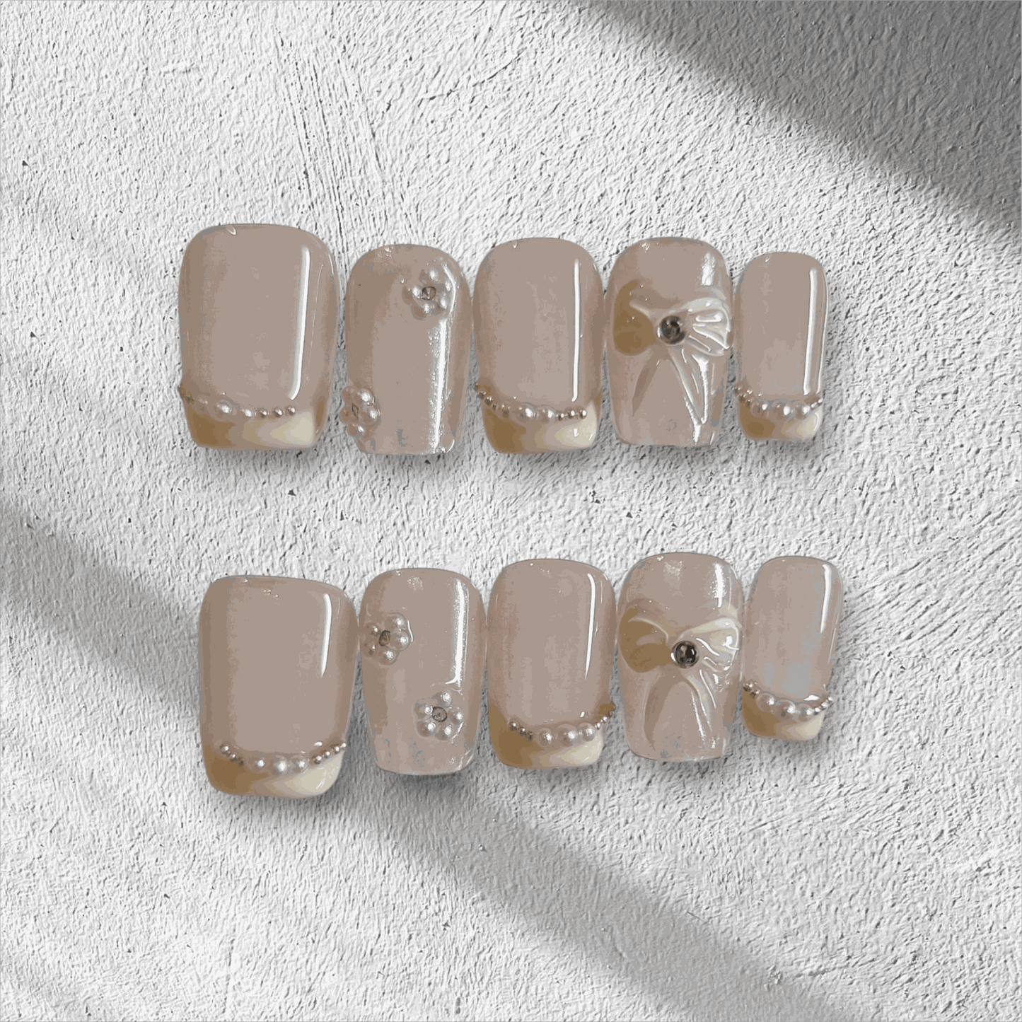 The Bahrain Bliss press-on nail set in a short square shape, featuring a nude base with 3D bows and pearl embellishments, perfect for a wedding.