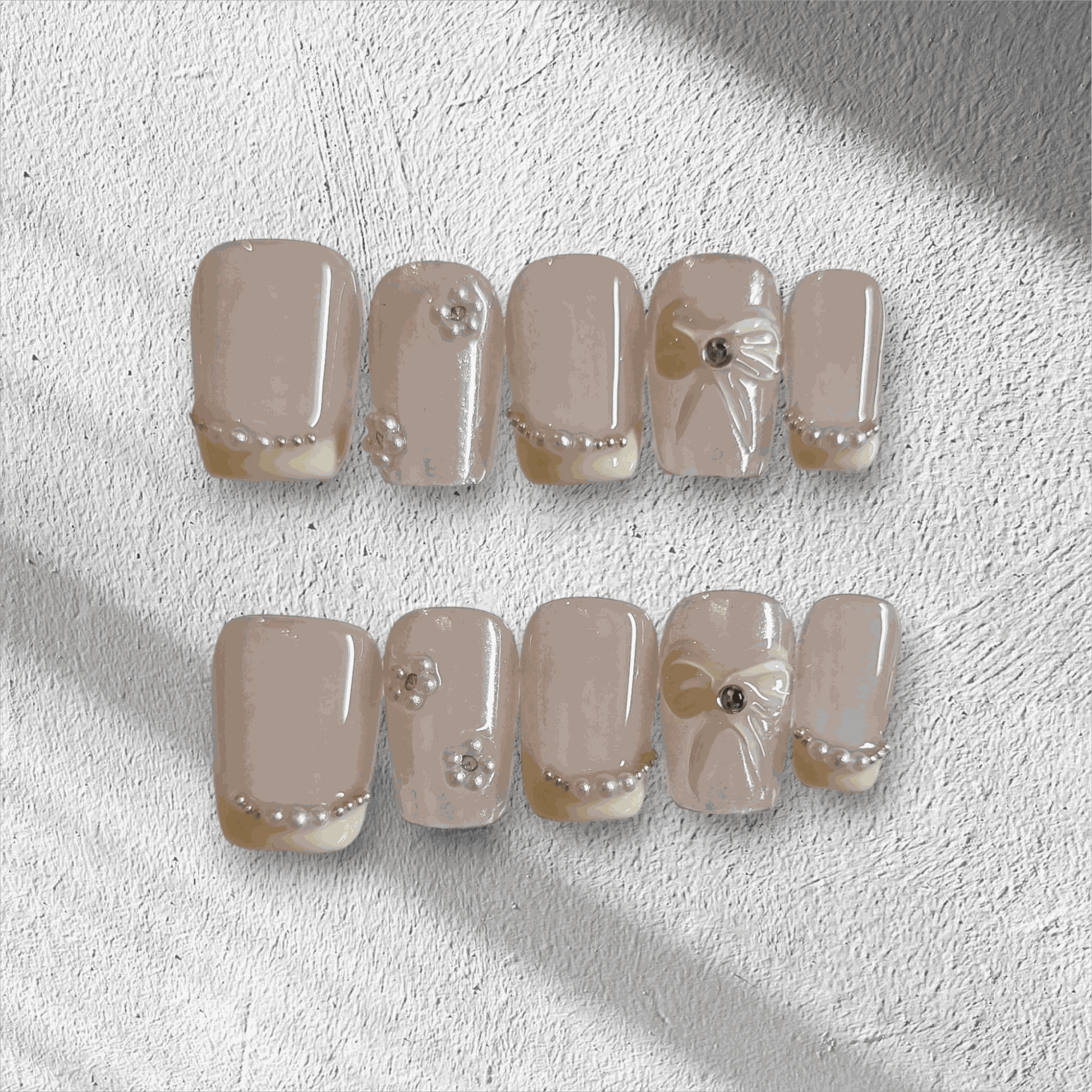 The Bahrain Bliss press-on nail set in a short square shape, featuring a nude base with 3D bows and pearl embellishments, perfect for a wedding.