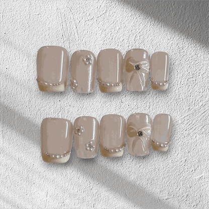 The Bahrain Bliss press-on nail set in a short square shape, featuring a nude base with 3D bows and pearl embellishments, perfect for a wedding.