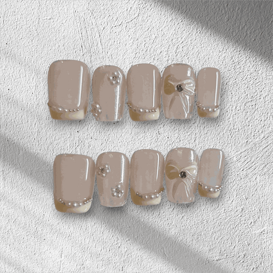 The Bahrain Bliss press-on nail set in a short square shape, featuring a nude base with 3D bows and pearl embellishments, perfect for a wedding.