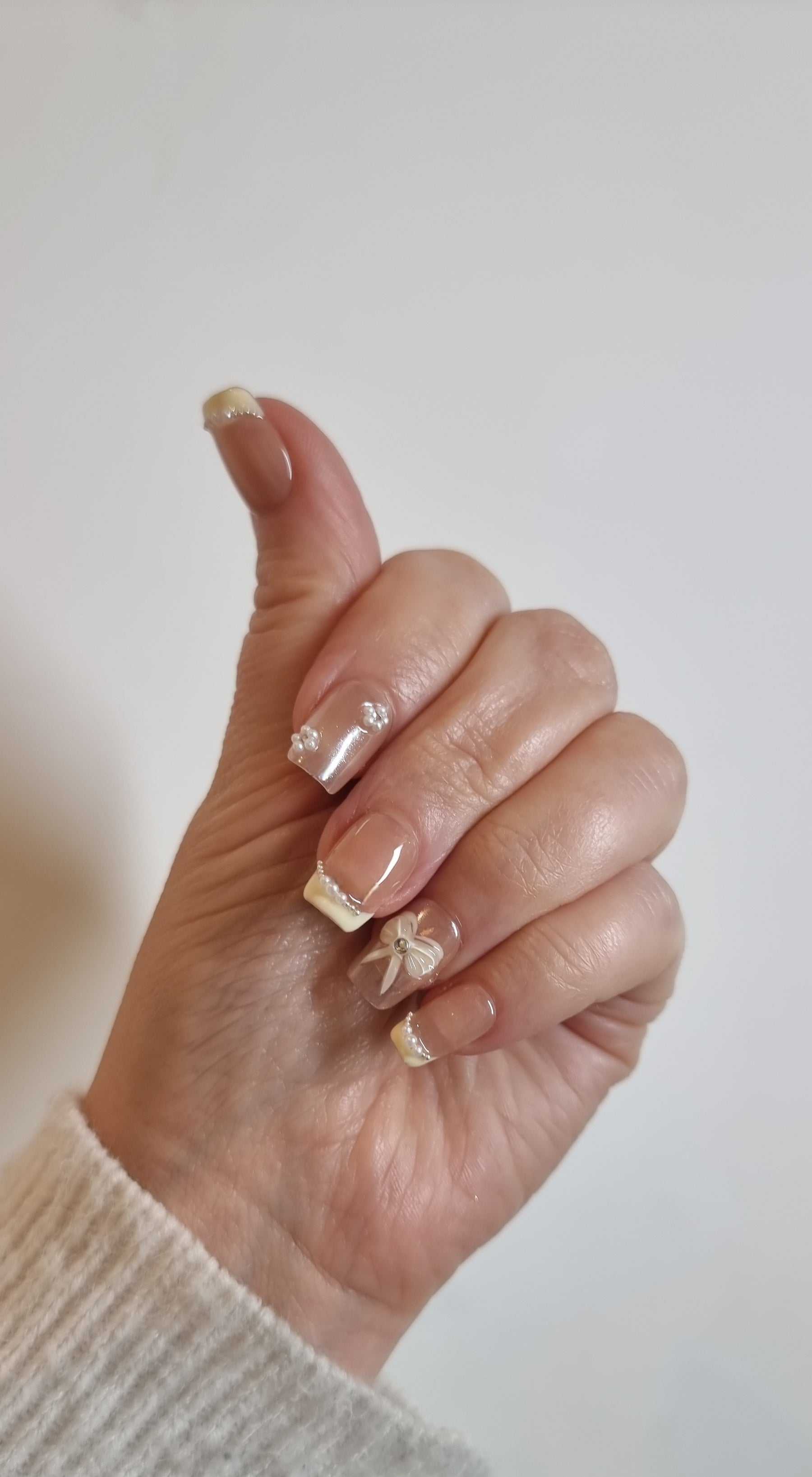 A model's hand wearing the elegant Bahrain Bliss press-on nails, showcasing the intricate 3D bow and pearl details.