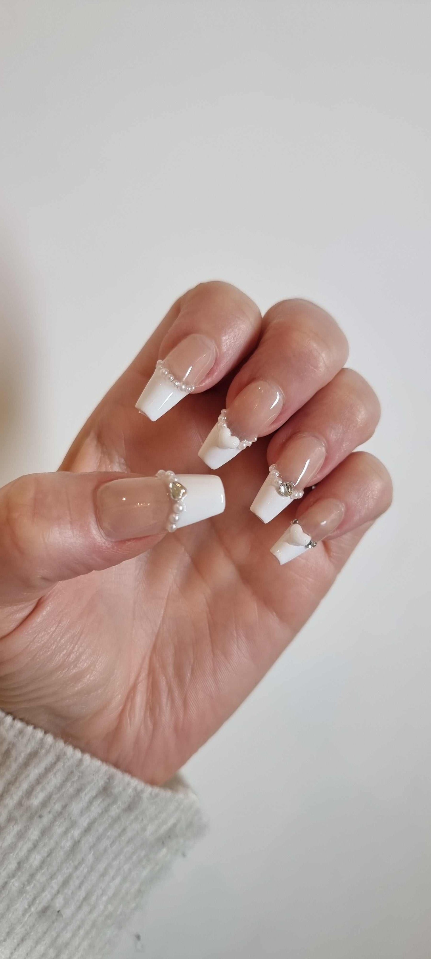 Model's hand wearing the Burj Beauty French manicure press-on nails, short square shape.