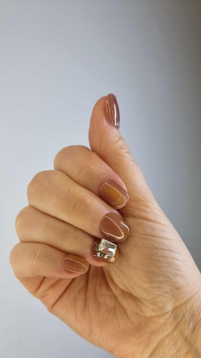 A model's hand wearing the elegant Bushra press-on nails, showcasing the stunning crystal accent nail and the warm nude color.