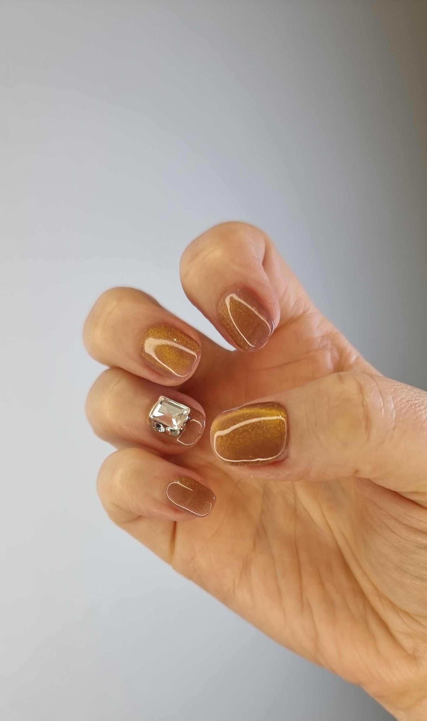 A model's hand wearing the elegant Bushra press-on nails, showcasing the stunning crystal accent nail and the warm nude color.