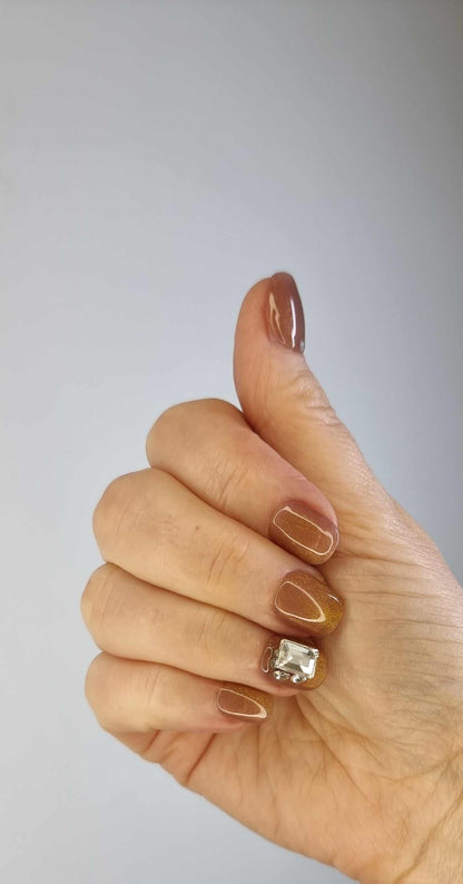 A model's hand wearing the elegant Bushra press-on nails, showcasing the stunning crystal accent nail and the warm nude color.