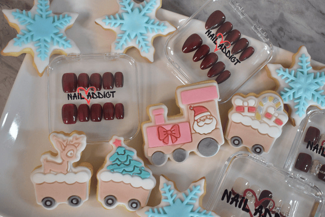 Decorative cookies shaped like a train, reindeer, and Christmas trees with nail polish packaging on a plate.