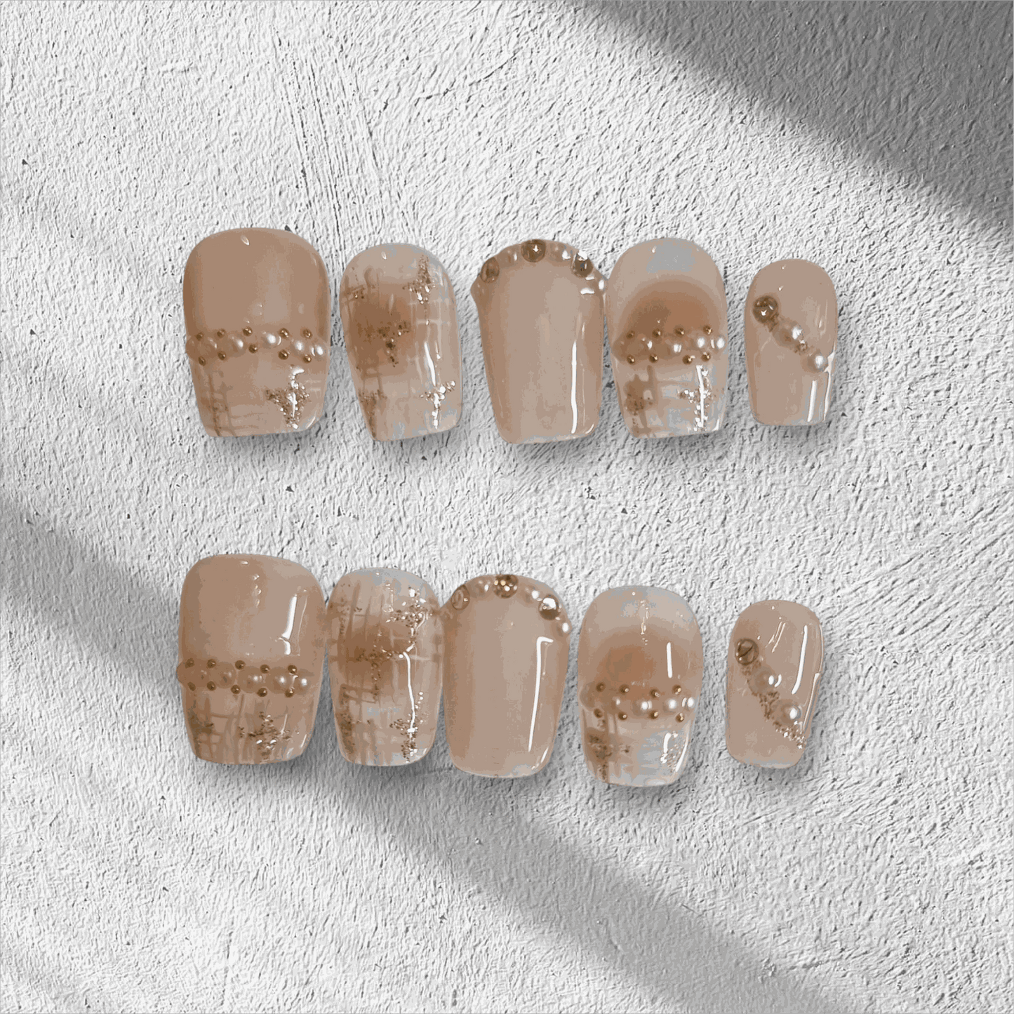 The Corniche Chic press-on nail set in a short square shape, featuring a nude base with delicate pearl and glitter line art details.